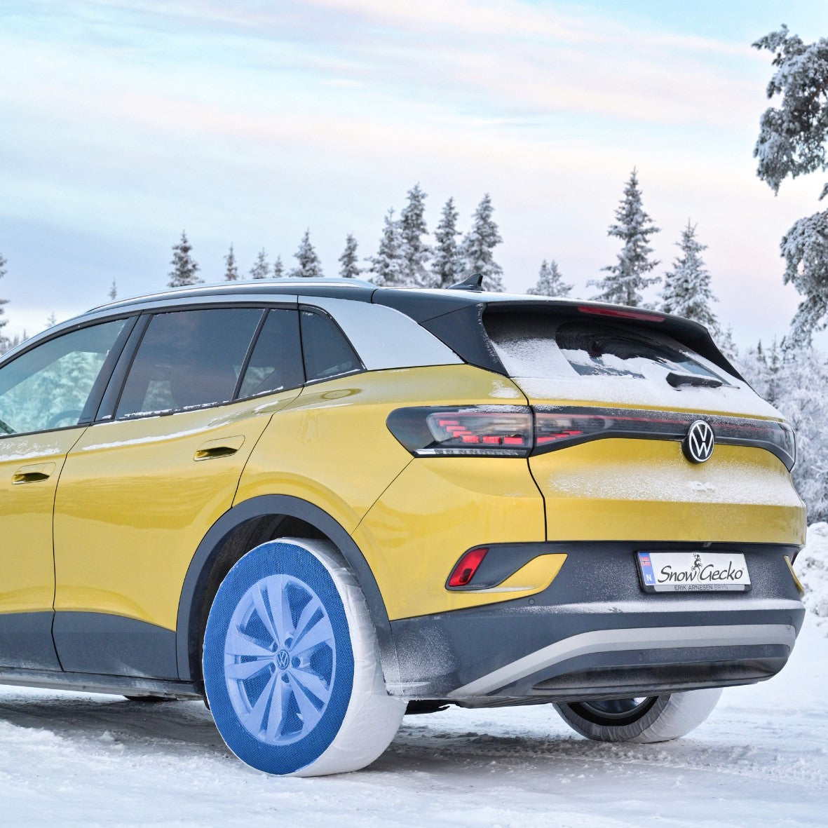 SnowGecko textile snow chains mounted on rear wheels of a yellow car, standing on snow