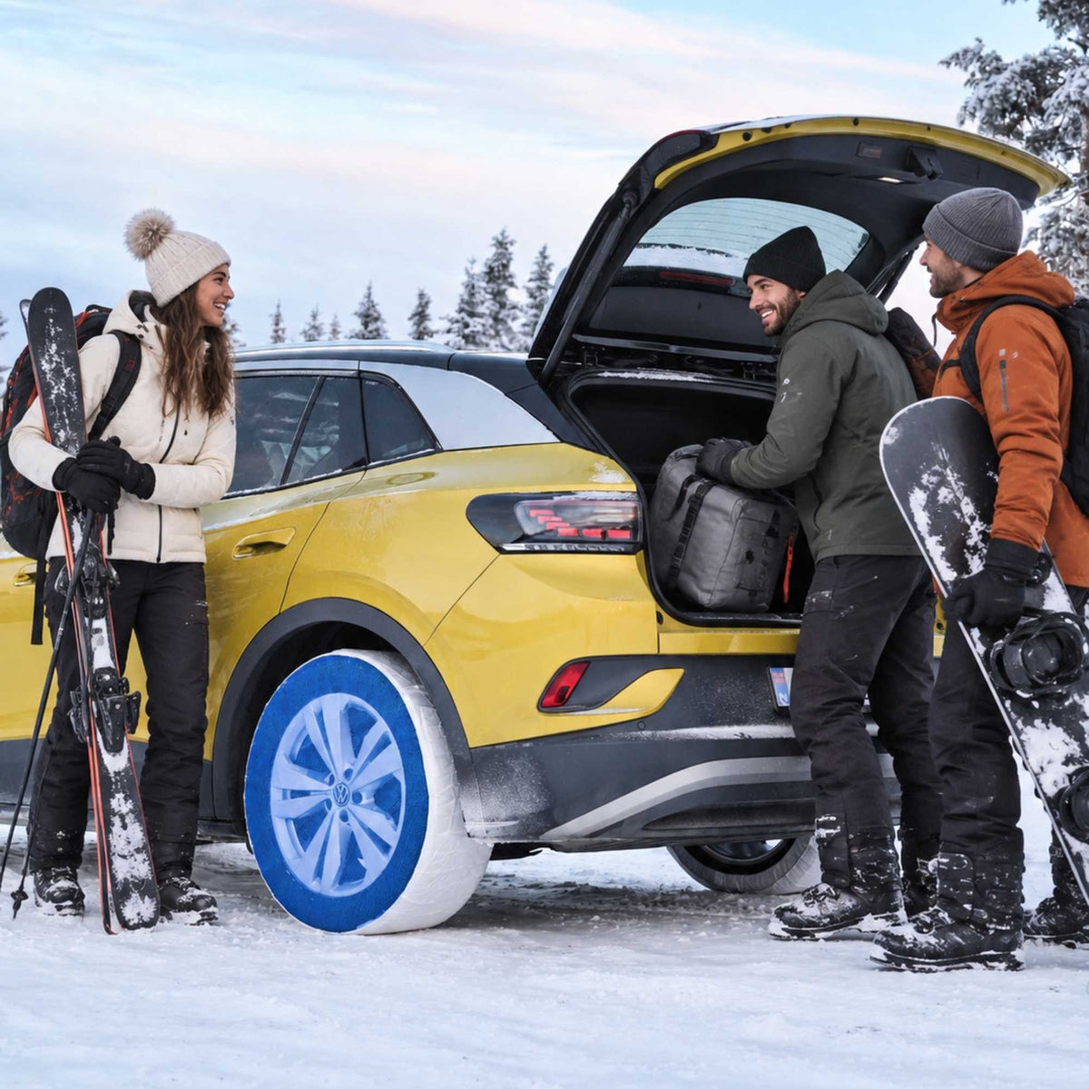 A bright yellow compact SUV with mounted snow socks is parked in the snow with three people around it, one loading gear into the open trunk and two holding snowboards. 
