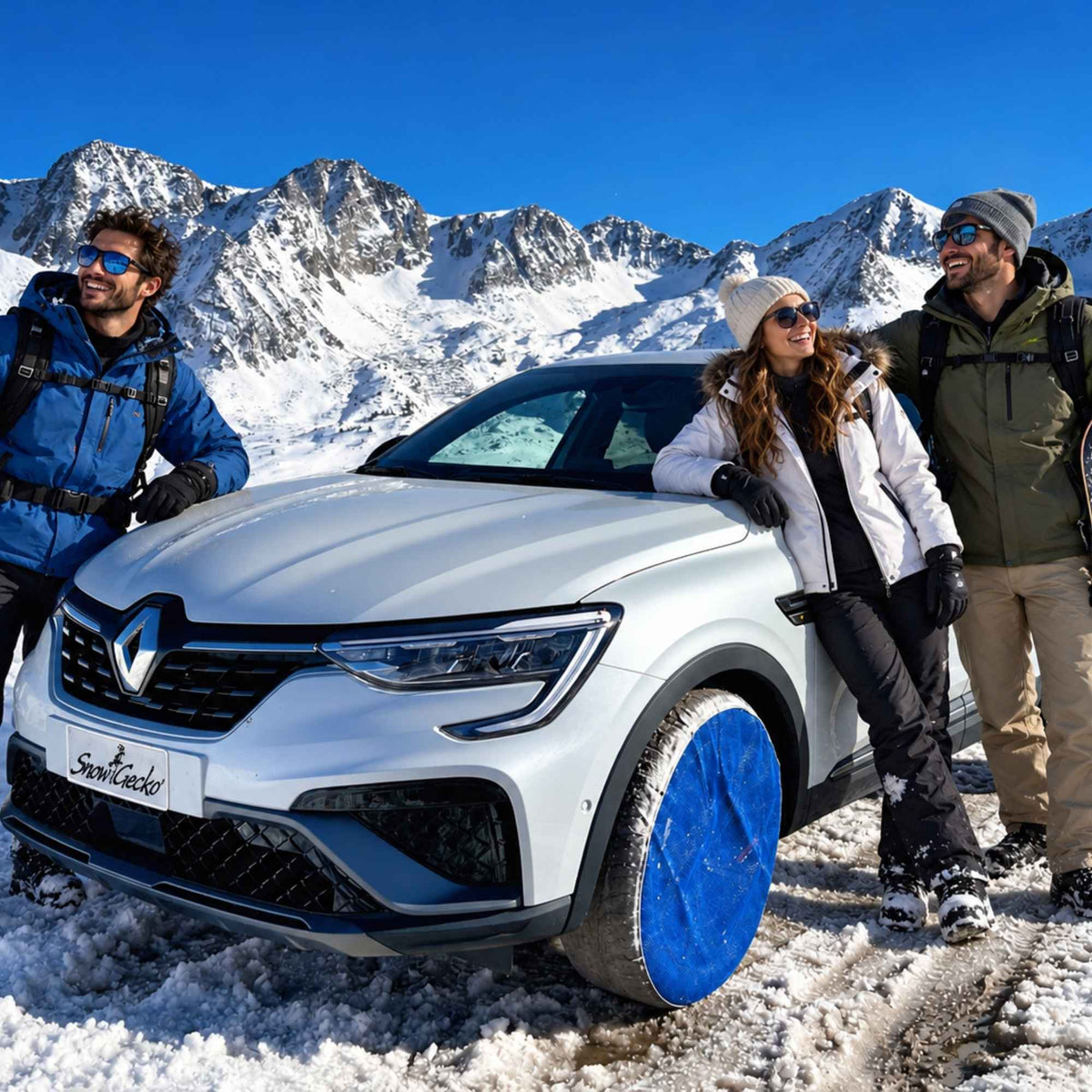 A gray Renault SUV parked in snowy mountains with three people posing beside it. The car has blue snow socks on the front wheel